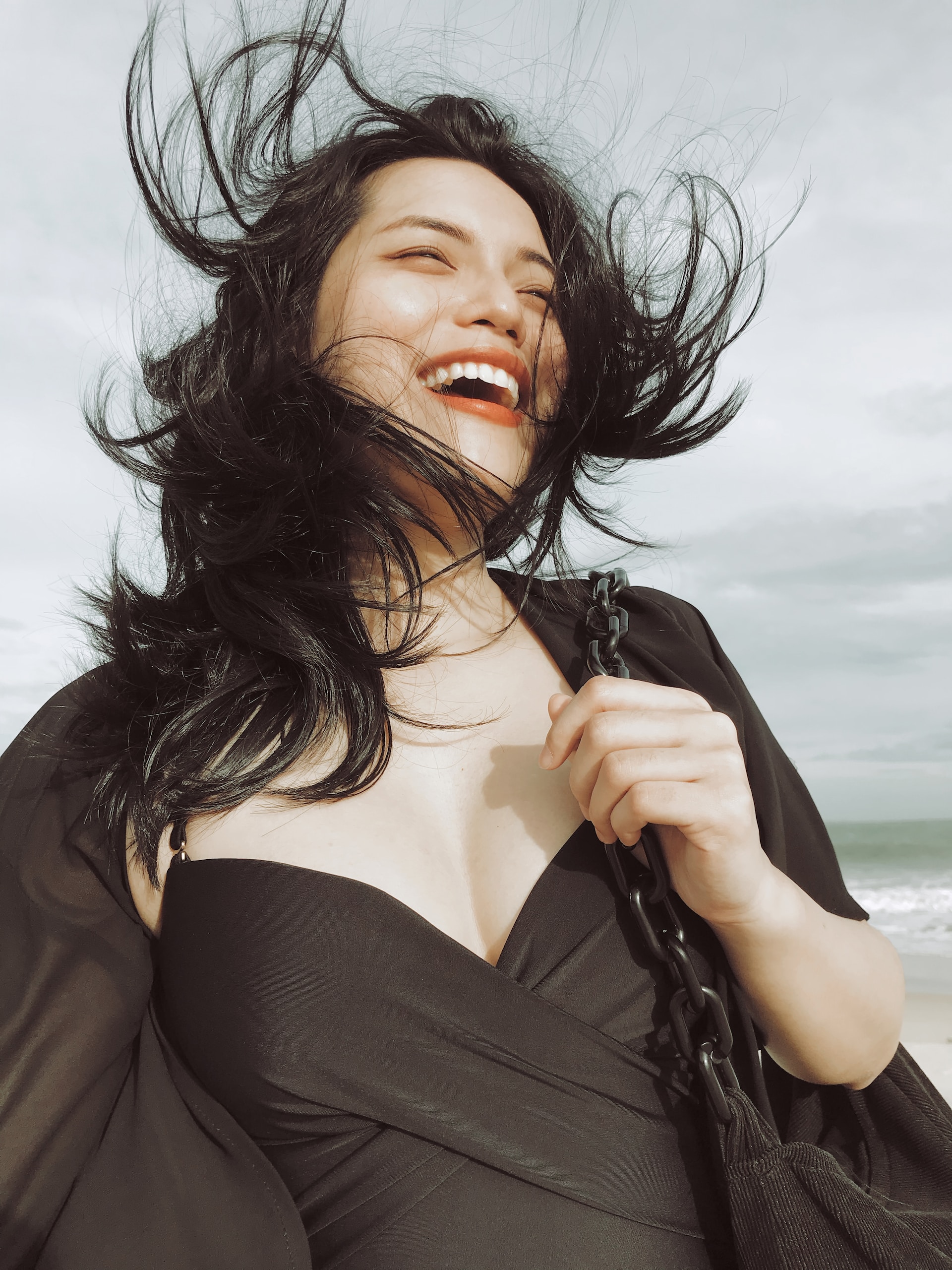 woman in black outfit smiling and laughing as wind blows through her hair