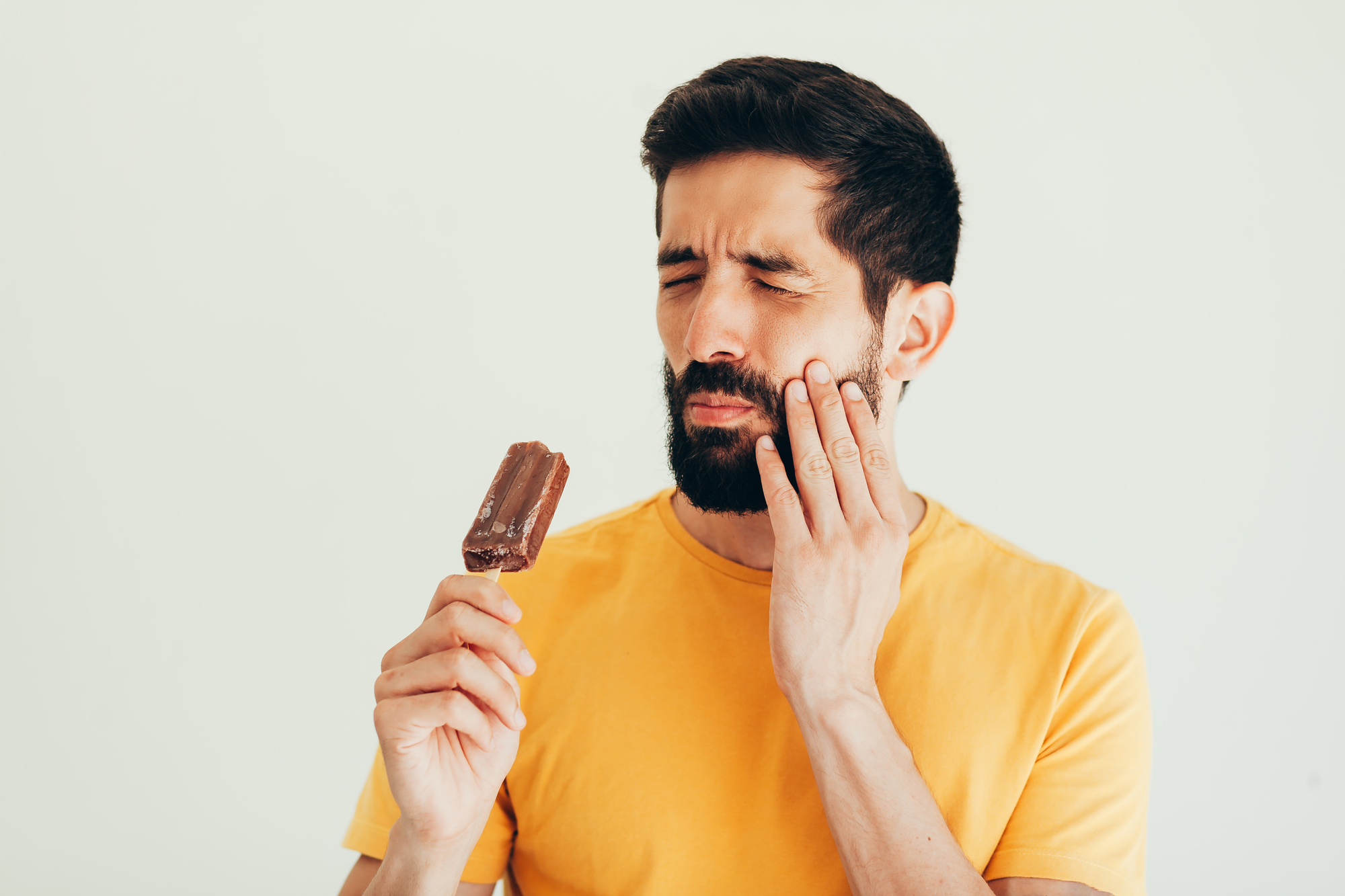 man wincing in pain while eating ice cream