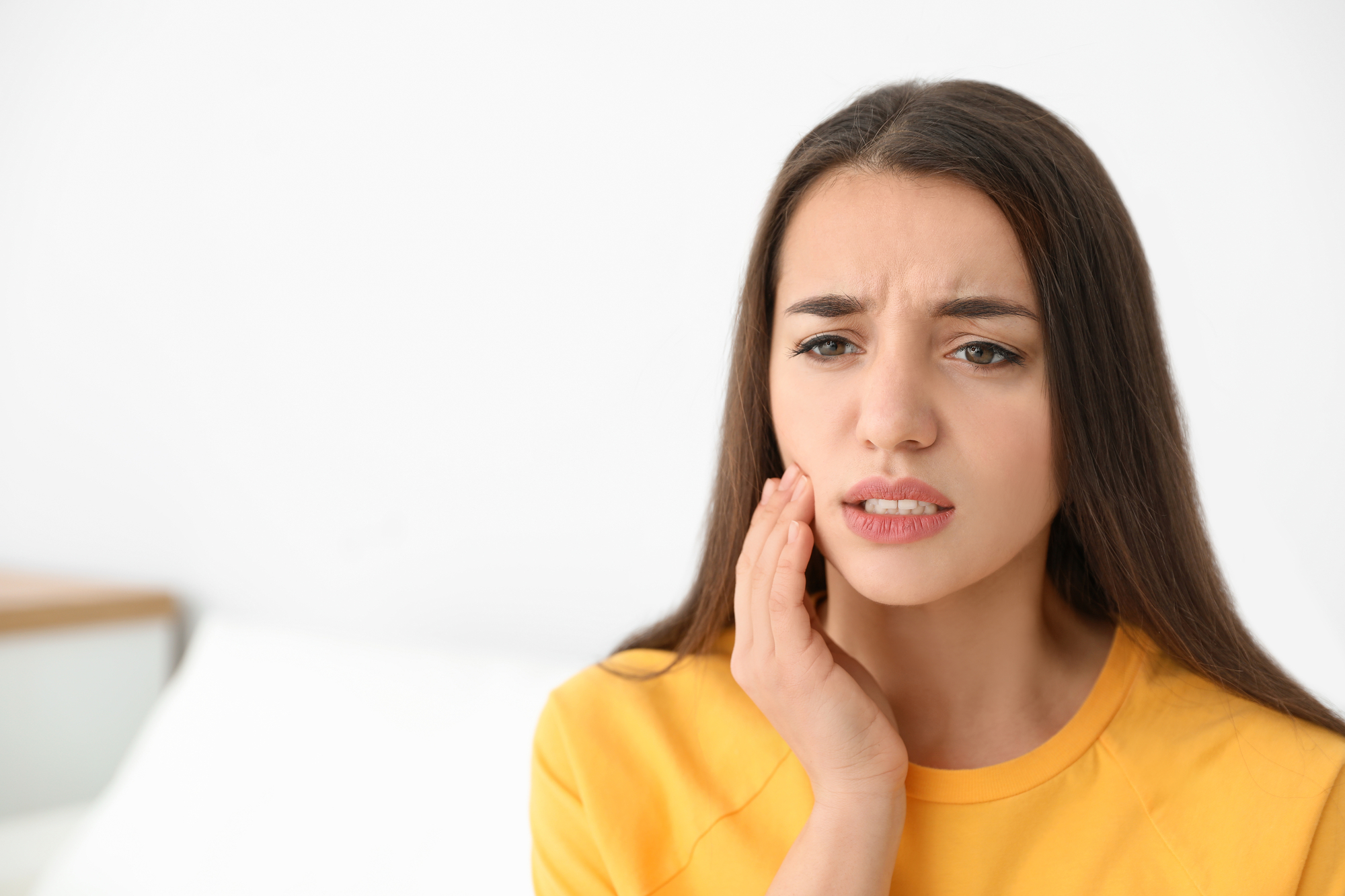 brunette woman in yellow sweater with Invisalign pain