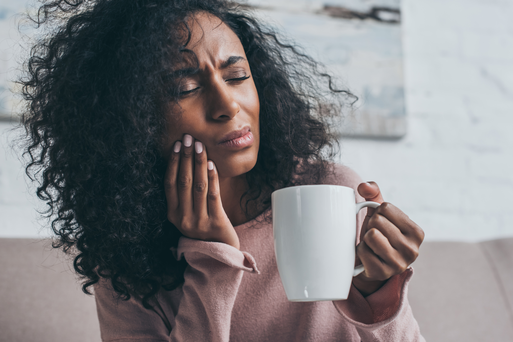 woman holding coffee cup and wincing from TMJ pain