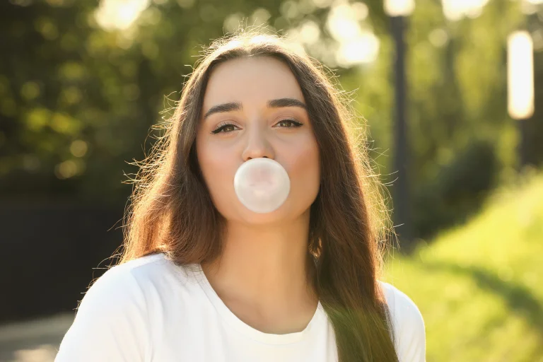young woman blowing a bubble with gum outside