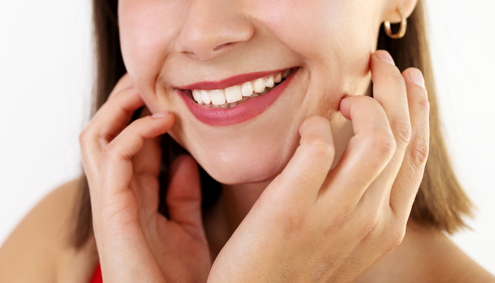 young woman smiling with hands near her face on white background