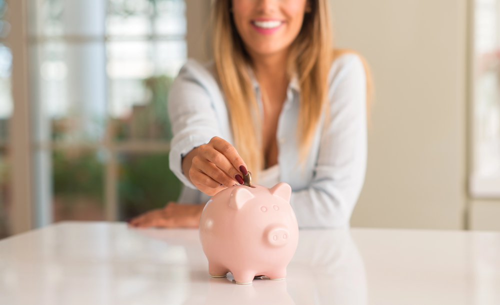woman placing coins in piggy bank, saving money for cosmetic dentistry