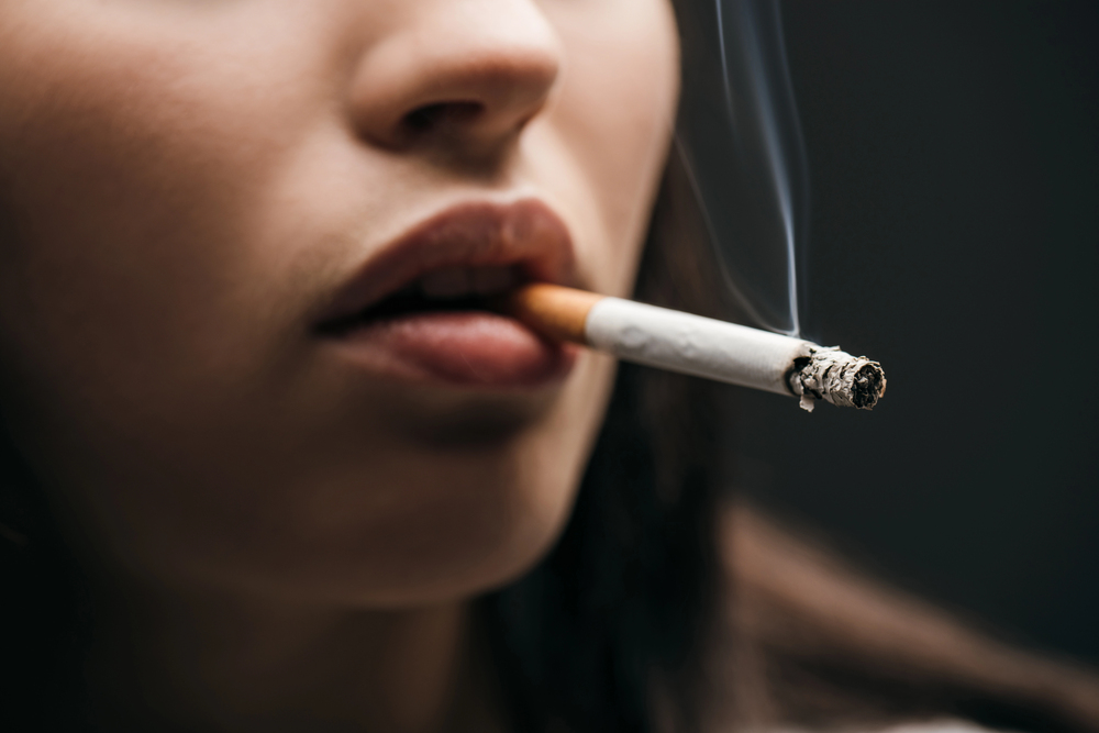 Selective focus of young woman smoking cigarette isolated on black