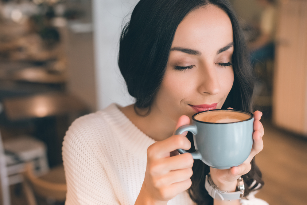 woman holding coffee mug up to her nose smelling and enjoying coffee in her home