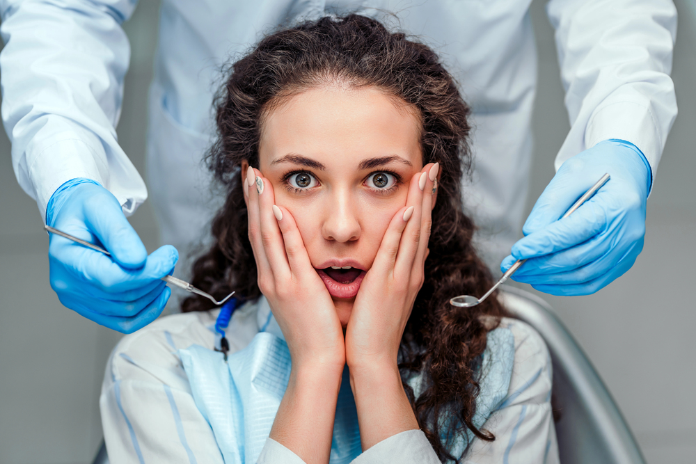 woman sitting in dentist chair holding her cheeks looking scared
