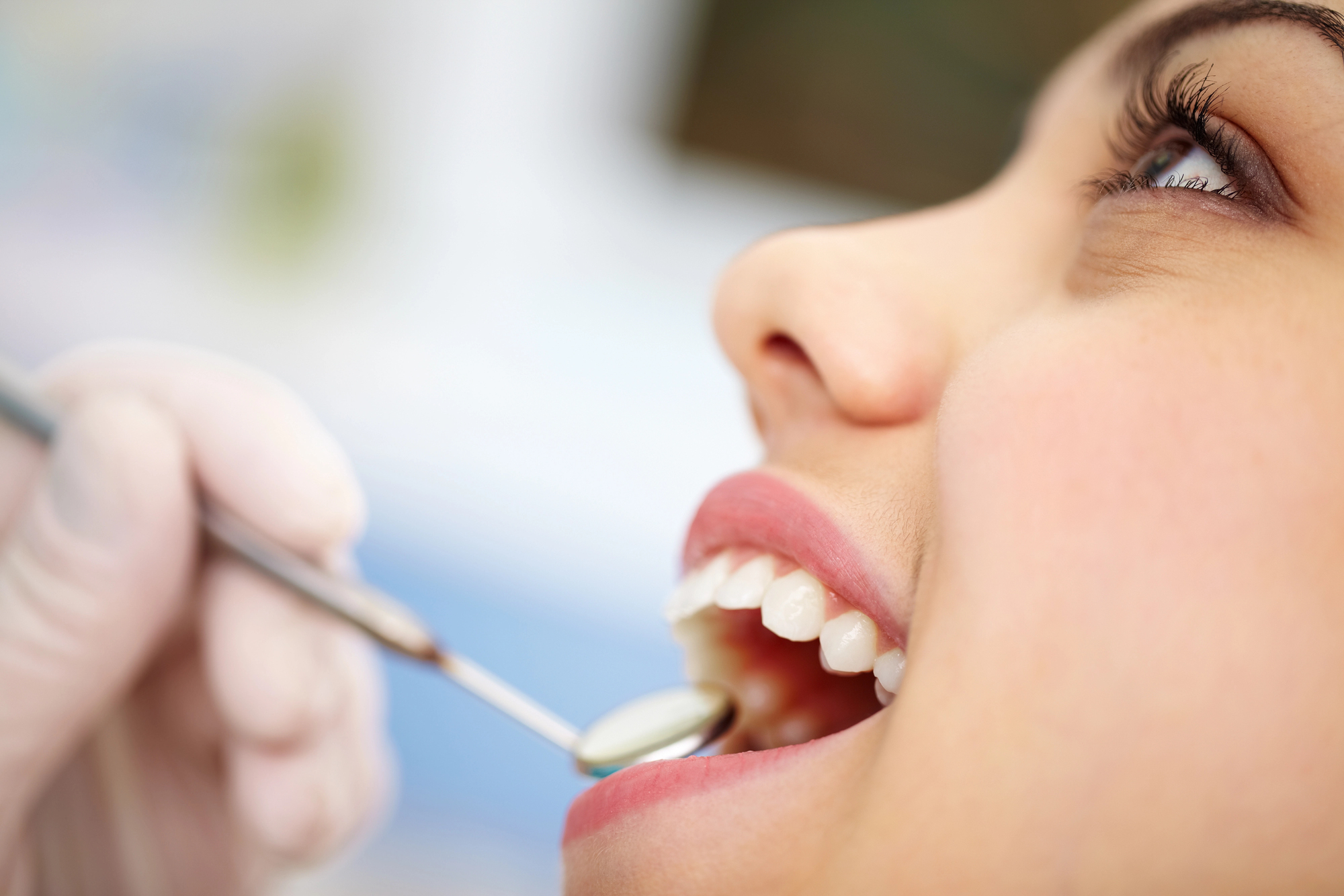 close up image of a dentist using a dental mirror to look inside a young lady's open mouth, depicting the answer to the question, "How has dentistry changed in 20 years?"