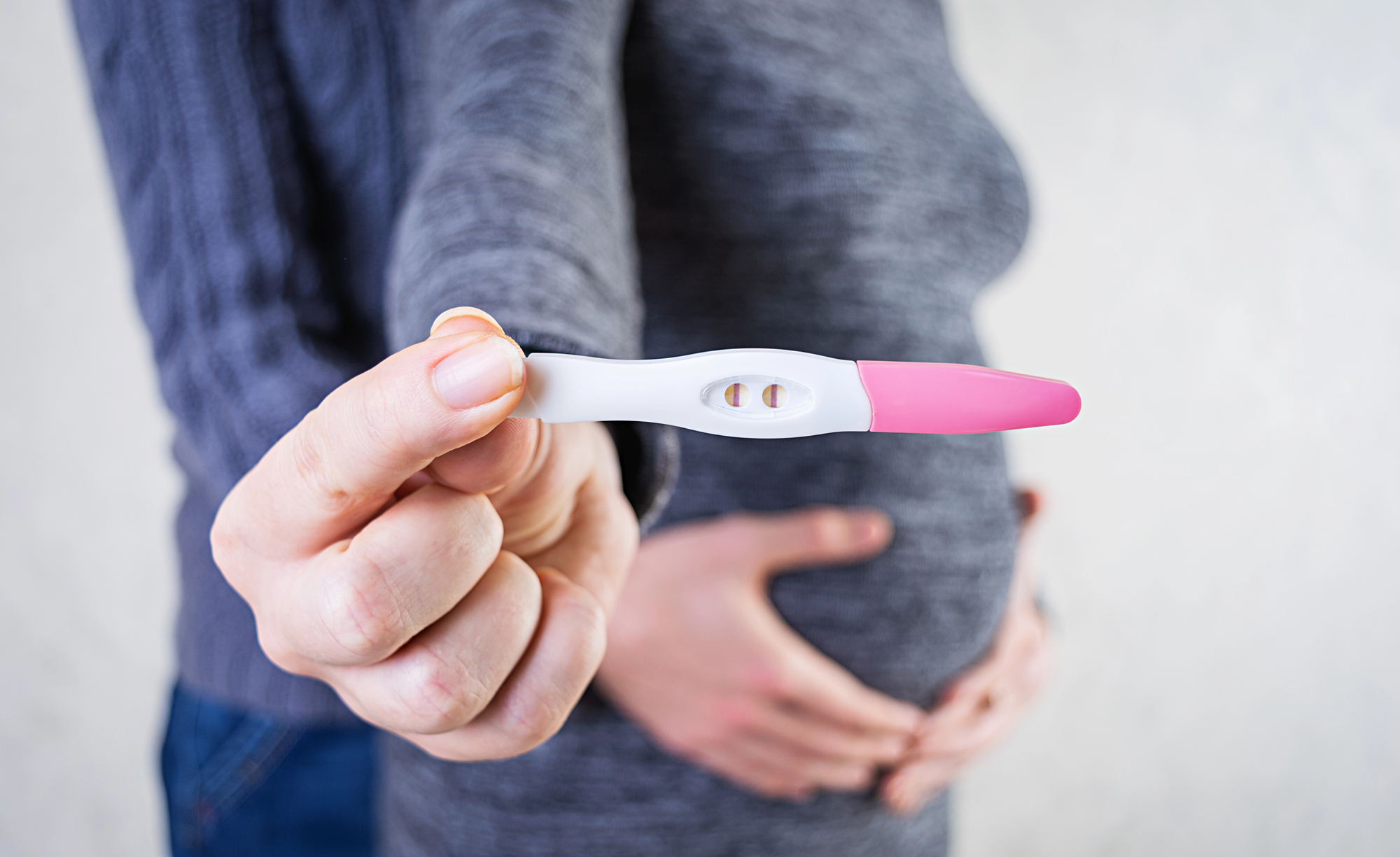 An image of a man cradling a woman's stomach as the woman holds up a positive pregnancy test after treating gum disease and increasing their fertility with a dentist in Las Vegas, NV