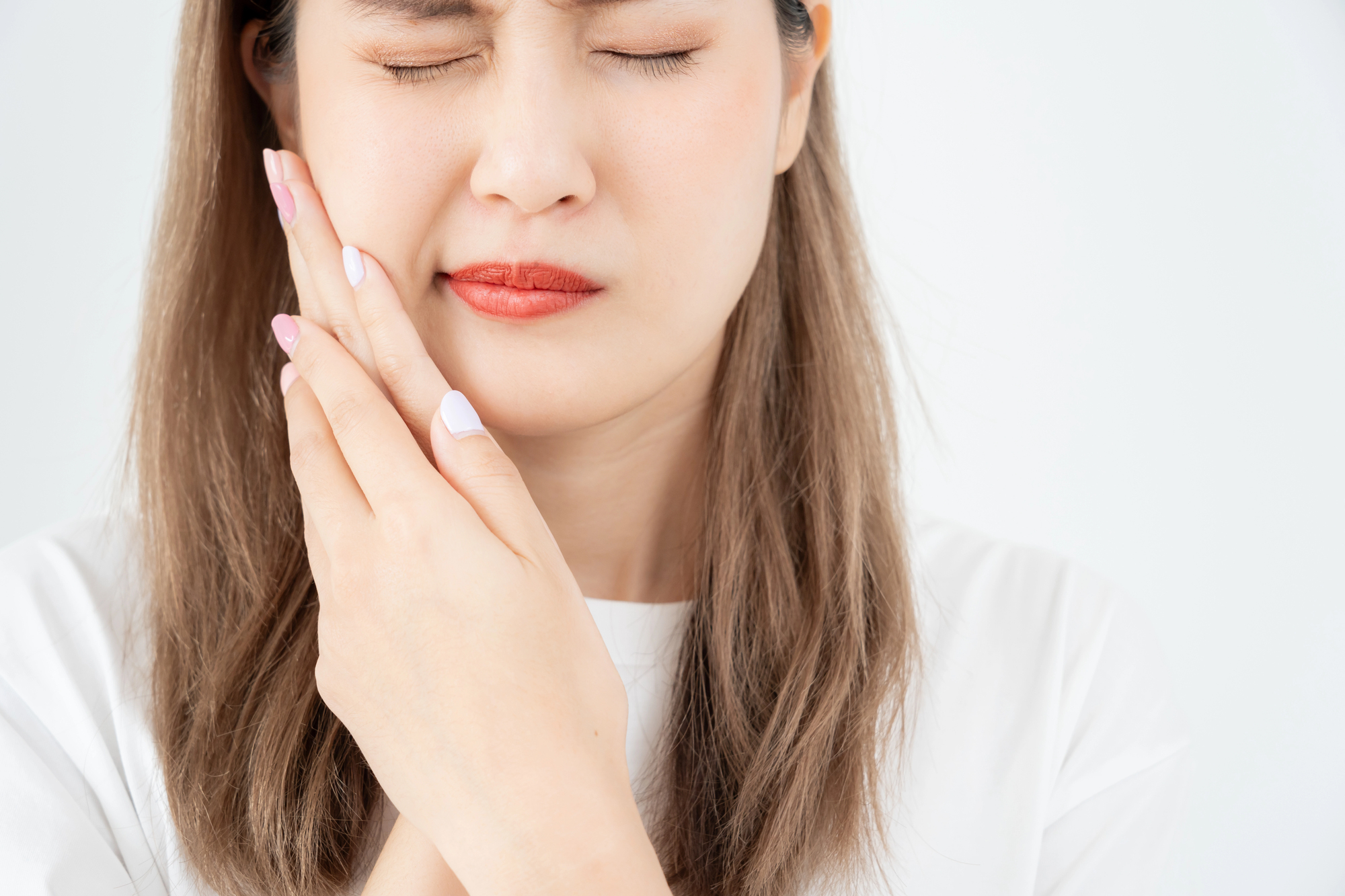 Asian woman clutches her right jaw, indicating that she has a toothache